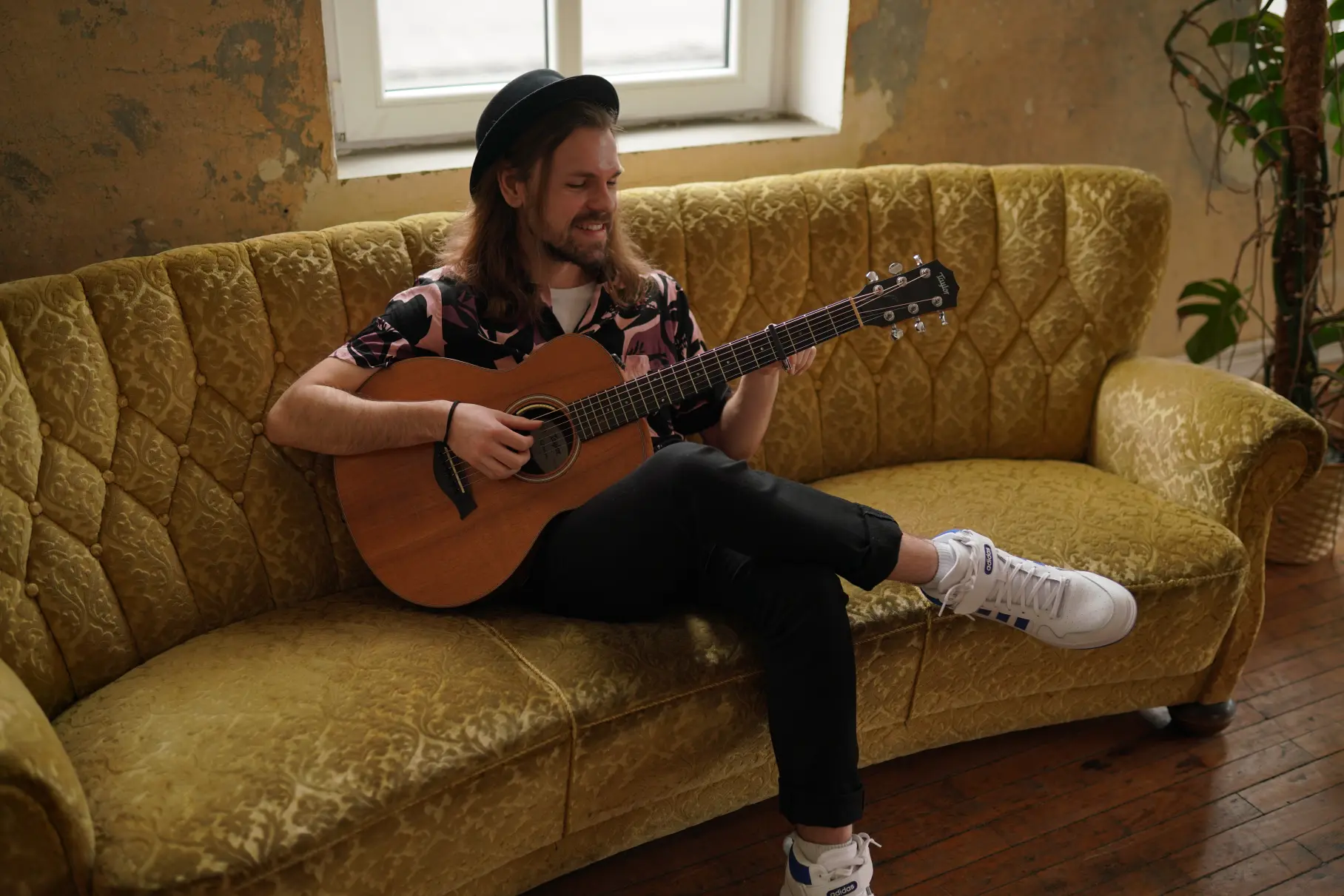 Sänger Will Church sitzt auf einer Couch in der Zimtlocation und spielt auf einer Gitarre.