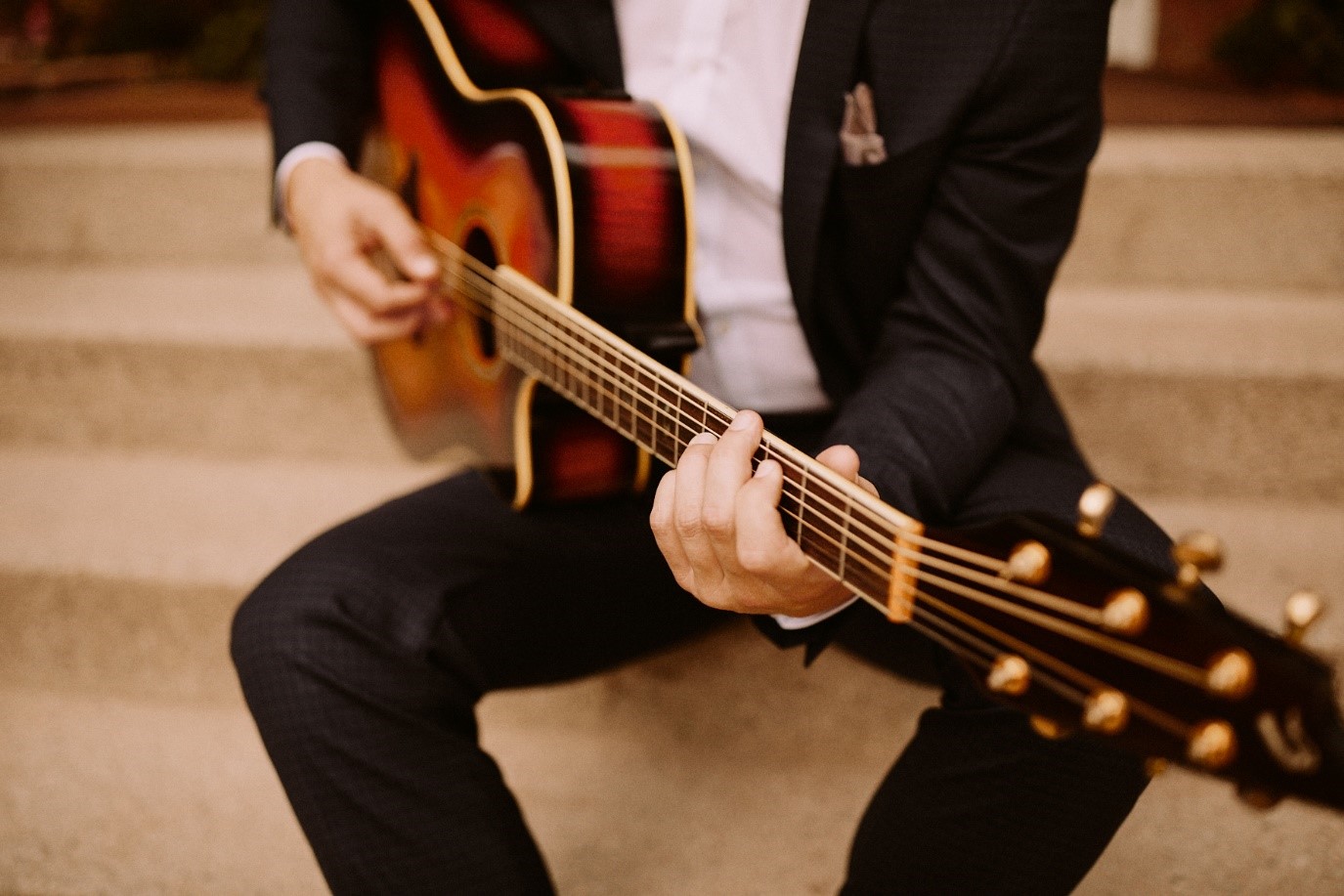 Musiker in Anzug hält eine schöne Gitarre in der Hand und sitzt auf einer Treppe.