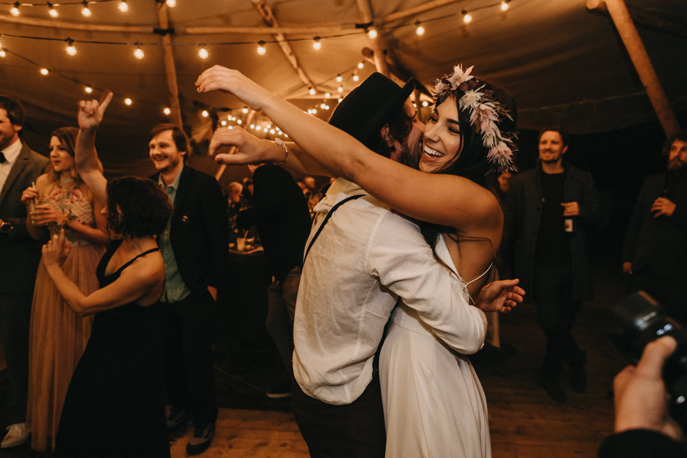 Hochzeitspaar umarmt sich beim Hochzeitstanz, im Hintergrund feiern die Gäste mit.